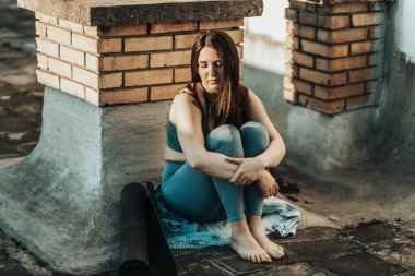 Young woman in depression sit with embrace knees lost in bad pessimistic thoughts and preparing for training on a rooftop terrace.