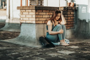 Young woman in depression sit with embrace knees lost in bad pessimistic thoughts and preparing for training on a rooftop terrace.