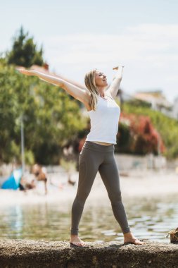 Fit middle age woman relaxing and enjoying summer day before doing training near the sea beach.