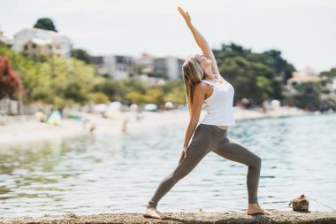Orta yaşlı, formda bir kadın, deniz kıyısındaki eğitim sırasında yoga egzersizi yapıyor..