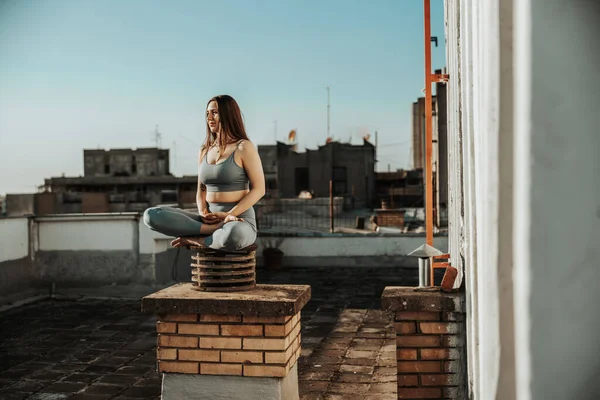 Relaxed woman practicing yoga meditating on a rooftop terrace.