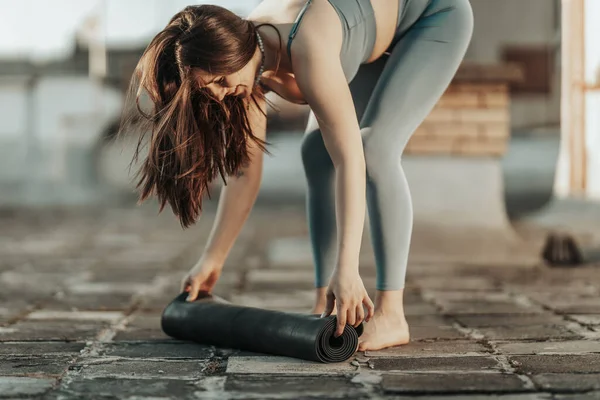 Relaxed woman is rolling up exercise mat and preparing to practicing yoga on a rooftop terrace.