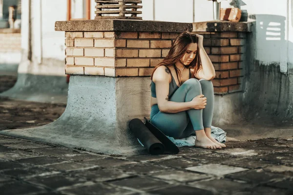 Young woman in depression sit with embrace knees lost in bad pessimistic thoughts and preparing for training on a rooftop terrace.