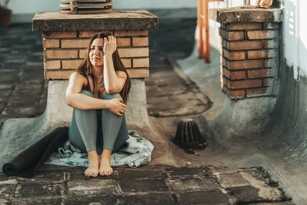 Young woman in depression sit with embrace knees lost in bad pessimistic thoughts and preparing for training on a rooftop terrace.