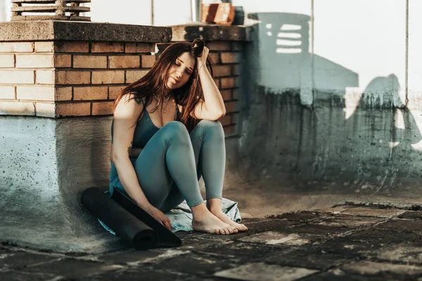 Lonely young woman in depression sit on a rooftop terrace lost in bad pessimistic thoughts after yoga training on a rooftop terrace.