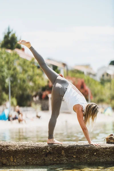 Fit middle age woman doing yoga exercises during training near the sea beach.