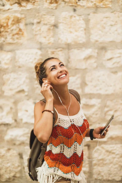 A young smiling woman enjoying music while exploring a Mediterranean city on a summer vacation.