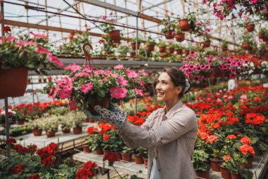 Smiling young woman working in a flower garden, holding and arranging flower pots.