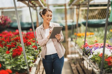 Young florist woman using digital tablet while working in a greenhouse.