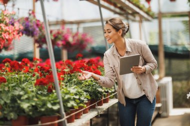 Young florist woman using digital tablet while checking flowers in a greenhouse. Woman entrepreneur.