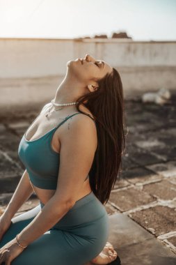 Rahat genç bir kadın terasta yoga yapıyor..