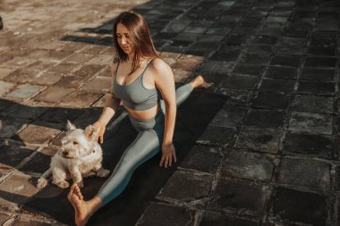 Relaxed woman practicing yoga stretching exercise on a rooftop supporting by her pet dog.