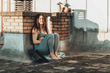 Young woman thinking of something while preparing for a yoga training on a rooftop terrace.