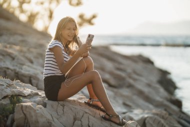 Cheerful teen girl having fun and enjoying music while spending summer day at the sea shore.