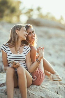 Two cheerful young women having fun while enjoying a summer vacation on a sea rock beach.