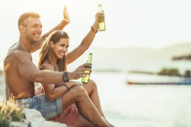 Young couple dancing and drinking beer on the beach party by the sea. Enjoying in beautiful sunset and their love.