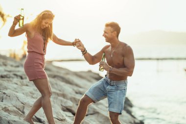 Young couple dancing and drinking beer on the beach by the sea.