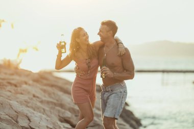 Young couple dancing and drinking beer on the beach by the sea. 