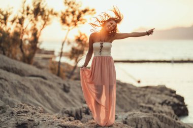 An attractive young woman dressed summer dress is having fun while spending sunset at the wonderful seaside.