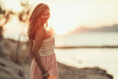 Portrait of an attractive young woman is having fun and enjoying summer sunset at the wonderful seaside.