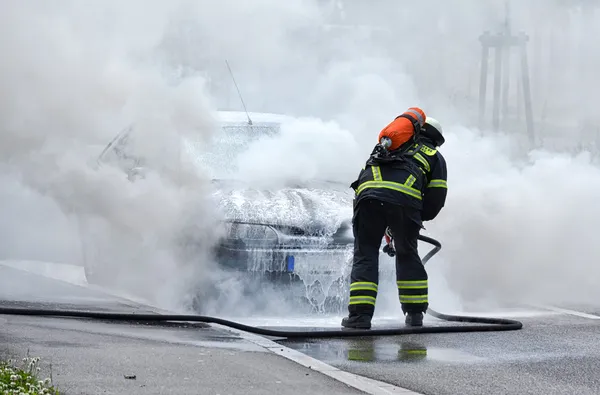 Tűzoltó kinyújtva egy égő autó — Stock Fotó