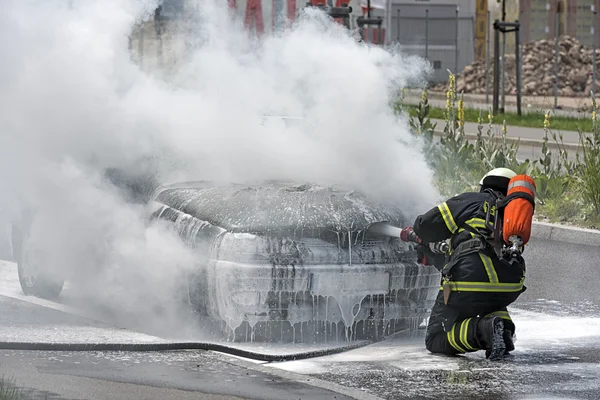 Tűzoltó kinyújtva egy égő autó — Stock Fotó