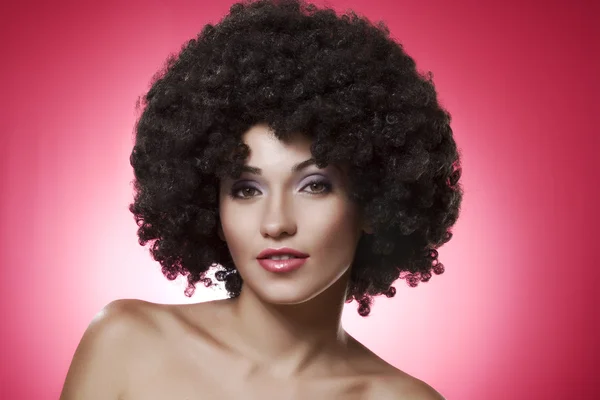 Close up portrait of young woman in afro wig on pink back — Stock Photo, Image