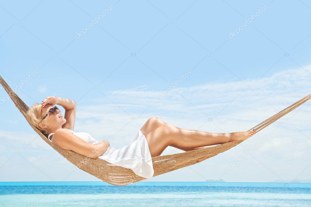 View of nice young lady swinging in hummock on tropical beach