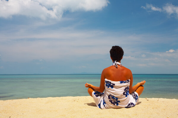 View of a woman meditating on the beach early in the morning