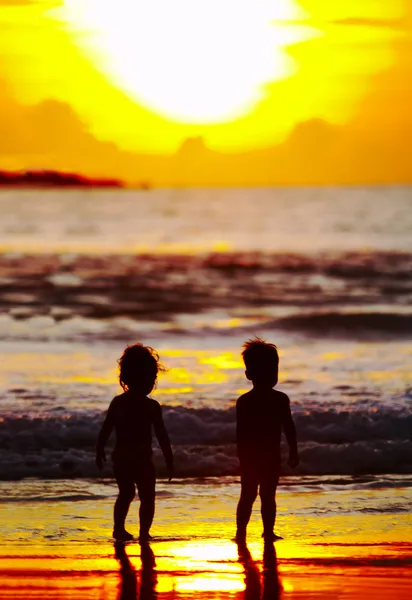 Visa på två barn silhuetter på stranden under solnedgången — Stockfoto