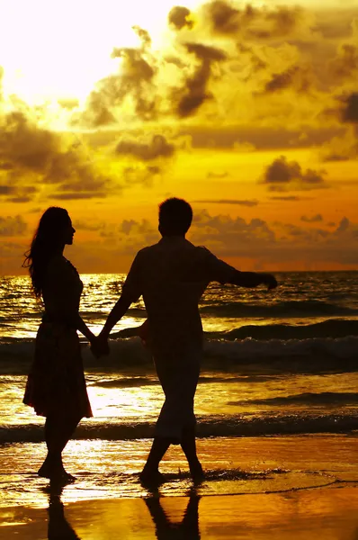Vista do jovem casal caminhando ao longo da costa durante o pôr do sol — Fotografia de Stock