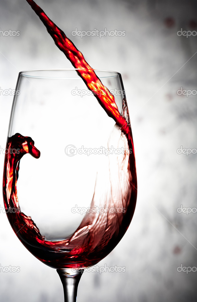 Close up view of wineglass getting filled with red wine on gray background