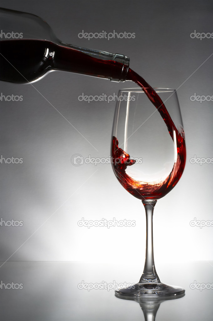 Red wine pouring into glass isolated on gray background