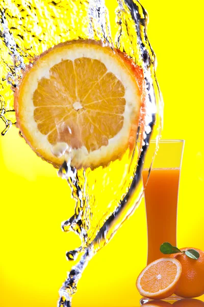 Vista de pedaço de laranja sendo espirrado e vidro de suco nas costas — Fotografia de Stock