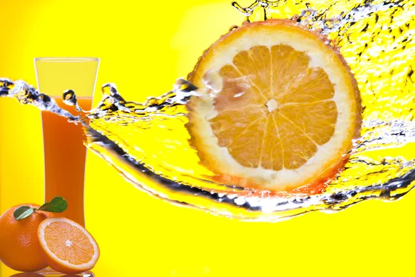 Vista de pedaço de laranja sendo espirrado e vidro de suco nas costas — Fotografia de Stock