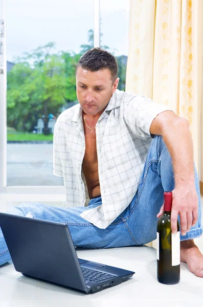 Retrato de jovem com uma garrafa de vinho e laptop — Fotografia de Stock