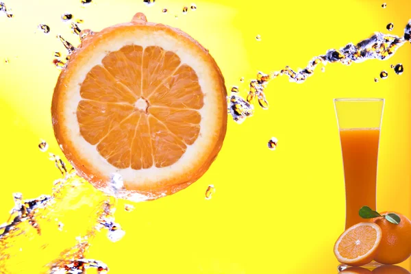 Vista del trozo de naranja salpicado y el vaso de jugo en la espalda — Foto de Stock