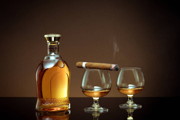  close up view of cigar, bottle of congnac and a glass aside on color back. 