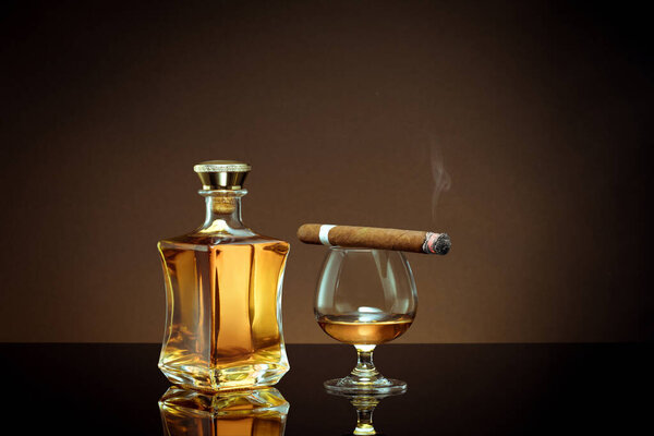 close up view of cigar, bottle of congnac and a glass aside on color back. 
