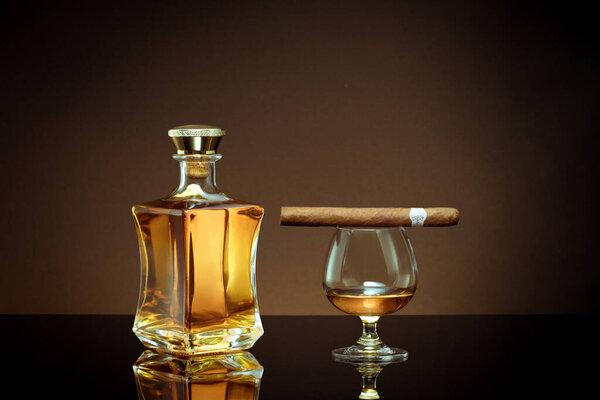 close up view of cigar, bottle of whiskey and  glass aside on color back. 