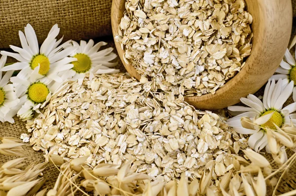 Oat flakes in a wooden bowl with chamomiles — Stock Photo, Image