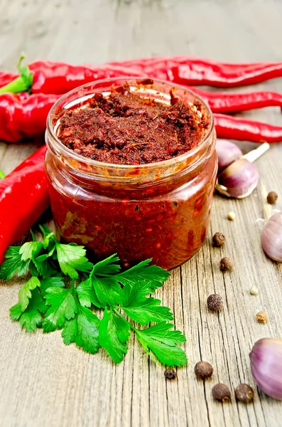 Ajika in a glass jar on the old board — Stock Photo, Image