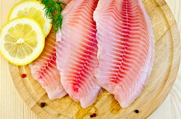 Fillets tilapia with lemon on a round board — Stock Photo, Image