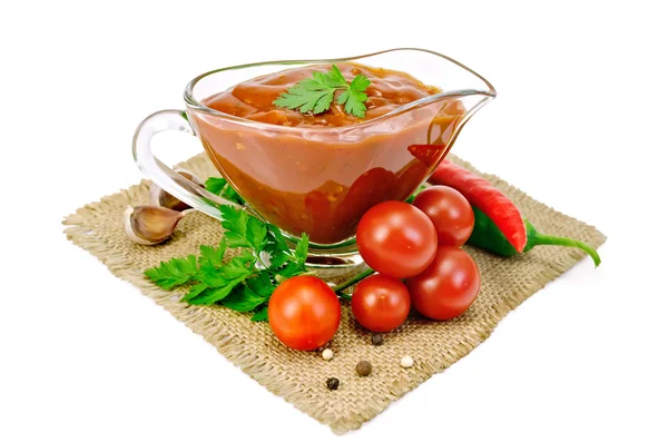 Ketchup in a glass gravy boat with vegetables on sacking — Stock Photo, Image