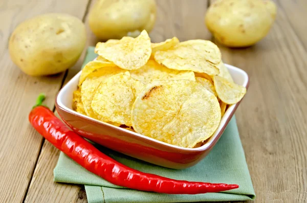 Chips in a bowl with hot peppers and potatoes on board — Stock Photo, Image