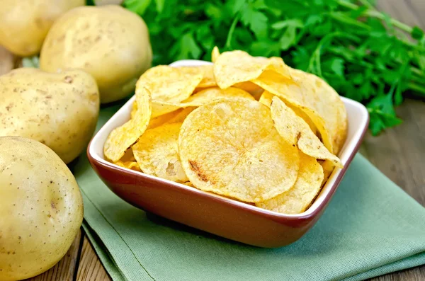 Chips in a bowl with a potato on the board and napkin — Stock Photo, Image