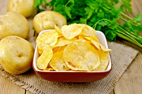 Chips in bowl with potatoes on sacking and board — Stock Photo, Image