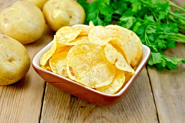 Chips in clay bowl with potatoes on board — Stock Photo, Image