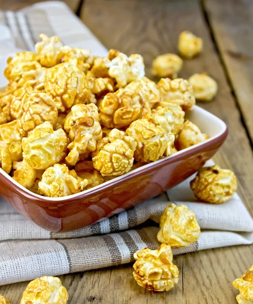 Popcorn caramel on board in clay bowl with napkin — Stock Photo, Image