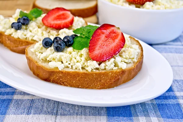 Bread with curd and berries on blue checkered cloth — Stock Photo, Image